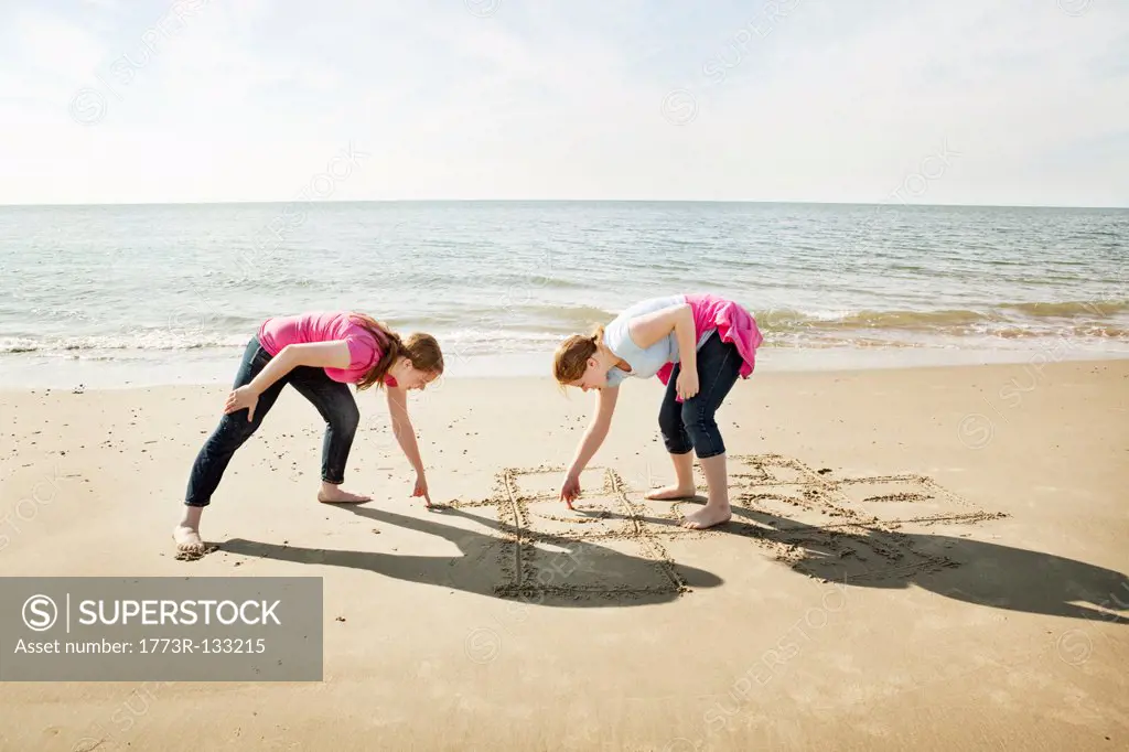 Girls drawing hopscotch in sand on beach