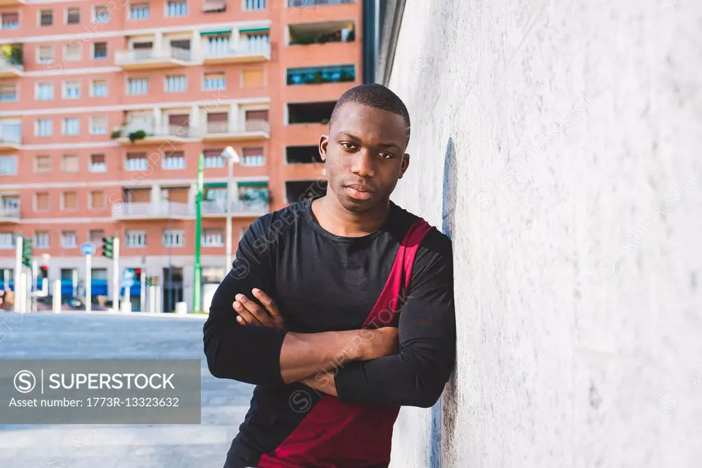 Portrait of young man leaning against wall, arms folded, pensive expression