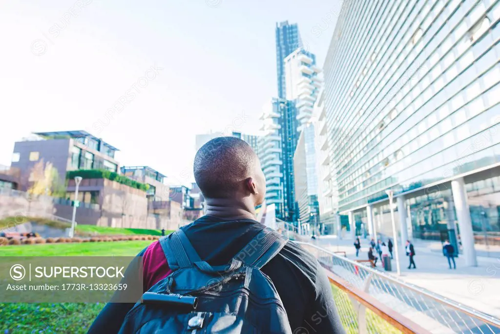 Young man walking outdoors, wearing backpack, rear view