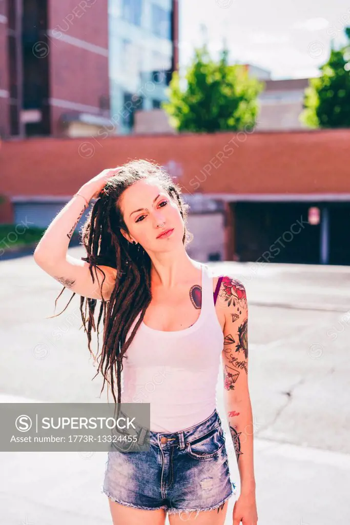 Young woman with hands in dreadlock hair in urban housing estate