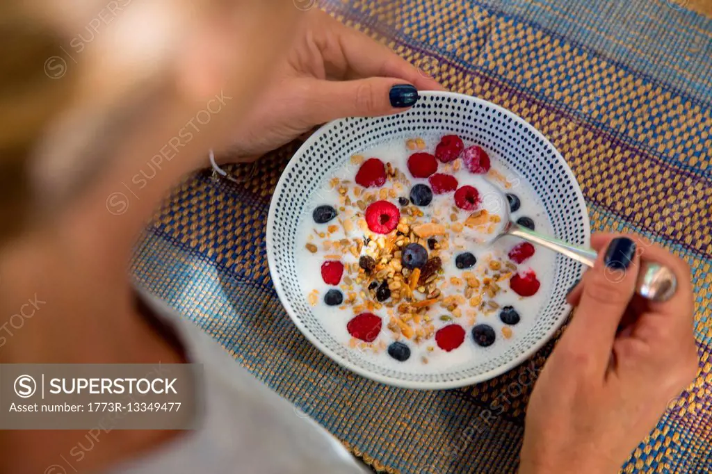Over shoulder view of woman eating cereal and berry breakfast