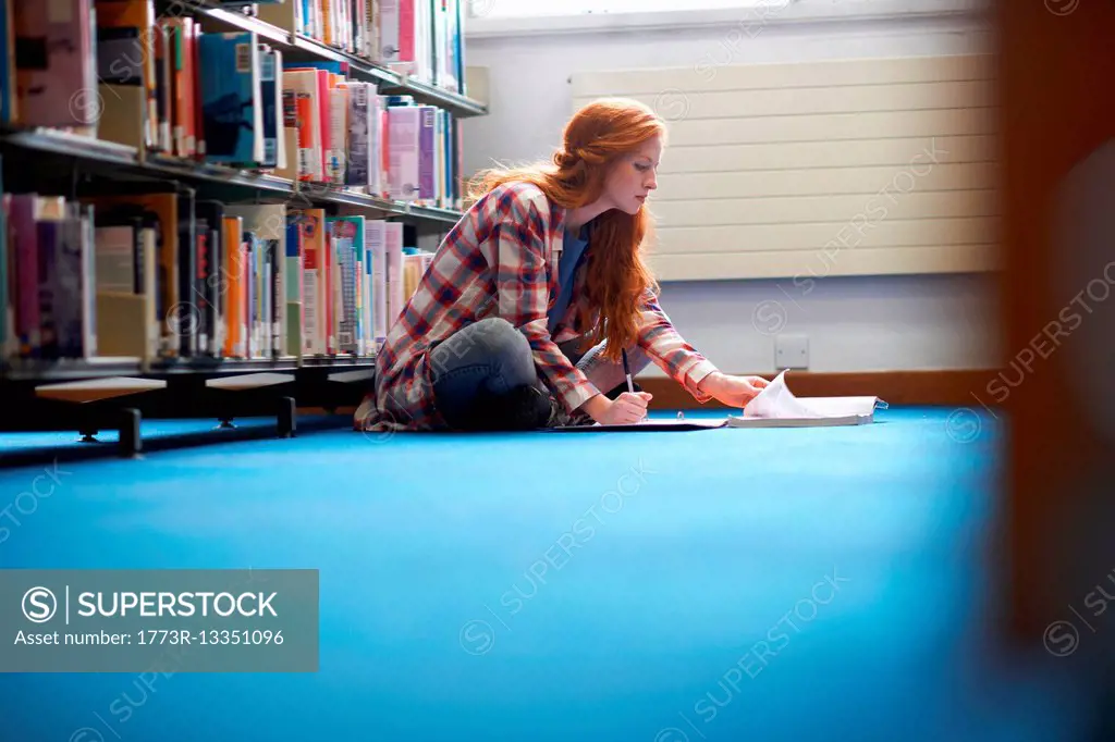 Young female college student writing notes on library floor