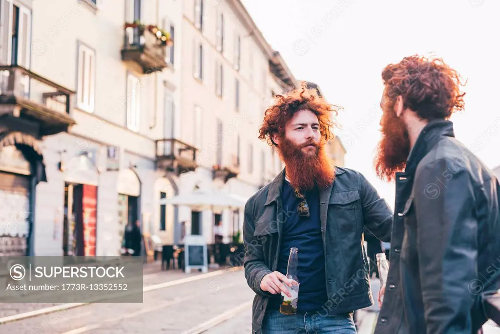 Young male hipster twins with red hair and beards talking on city street