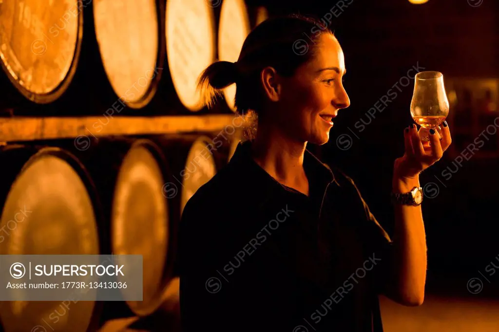 Female taster looking at the colour of whisky in glass at whisky distillery
