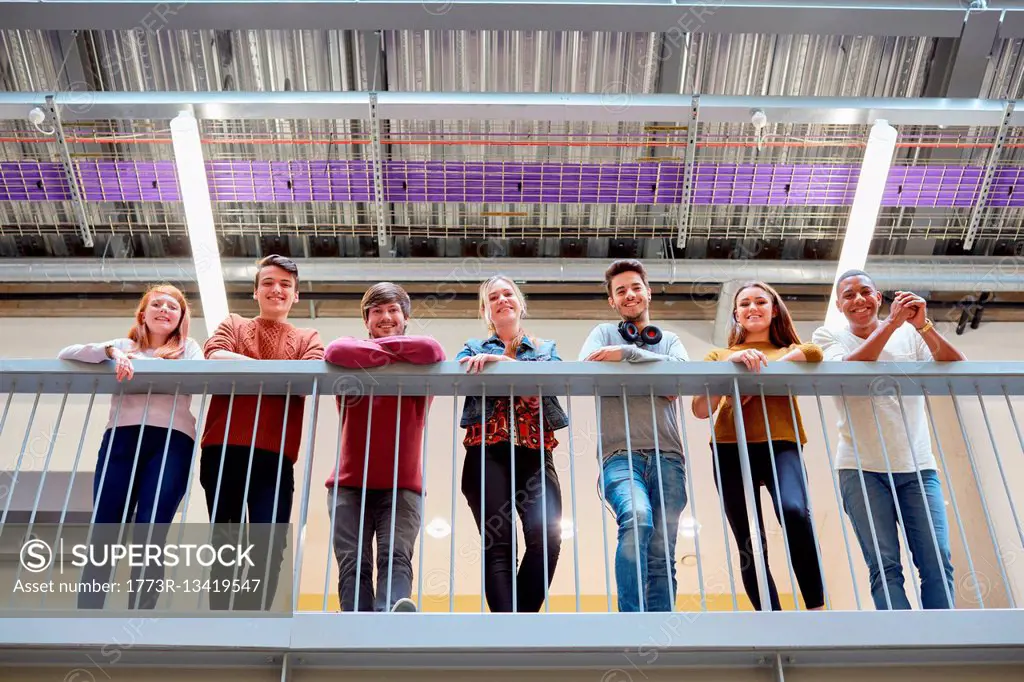 Portrait of male and female students looking down from balcony in higher education college