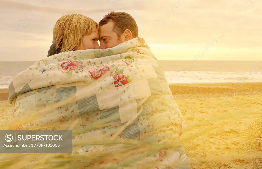 Couple cuddling under blanket on beach