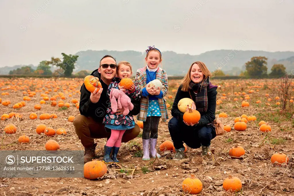Portrait of parents and two daughters crouching in pumpkin field