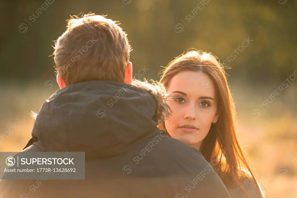 Young couple in field, young woman looking over man's shoulder
