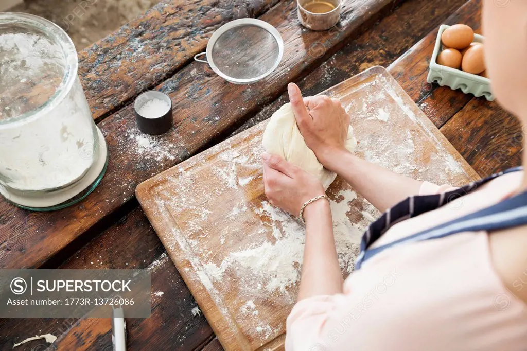 Over shoulder view of young woman kneading dough on chopping board