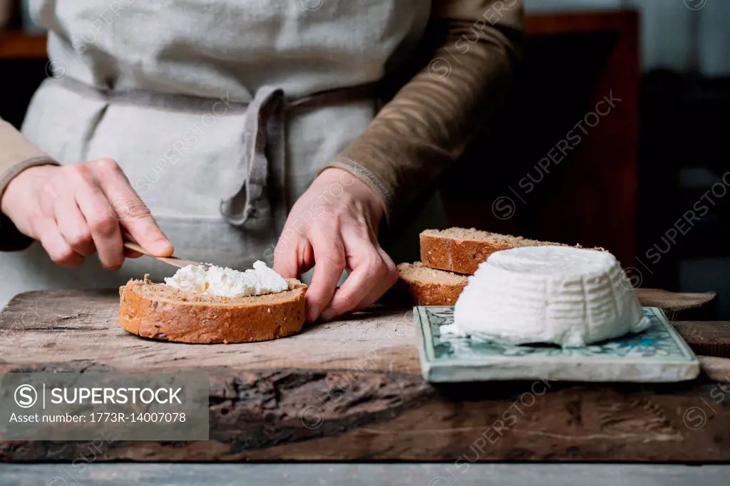 Woman spreading ricotta cheese onto slice of bread, mid section