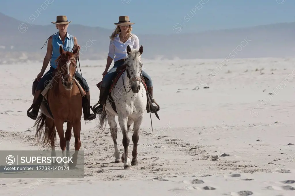 2 people riding horses on the beach