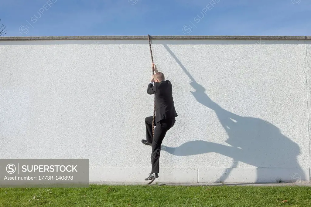 Businessman climbing over wall with rope