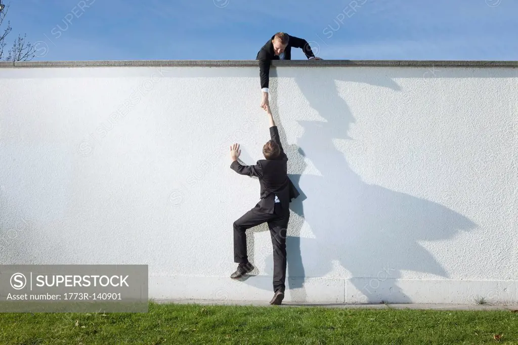Businessman pulling colleague over wall
