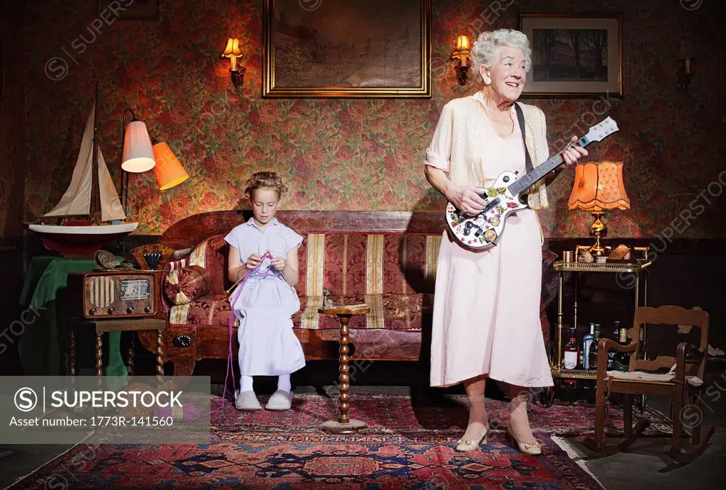 Older woman playing guitar as girl knits