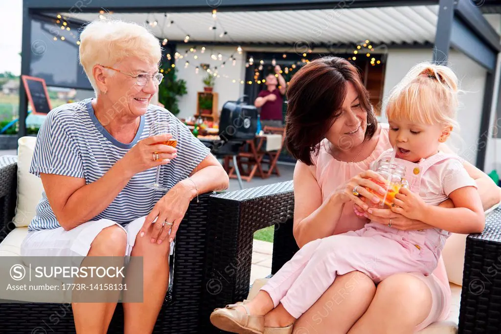 Senior and mature women with female toddler on lap at family lunch on patio