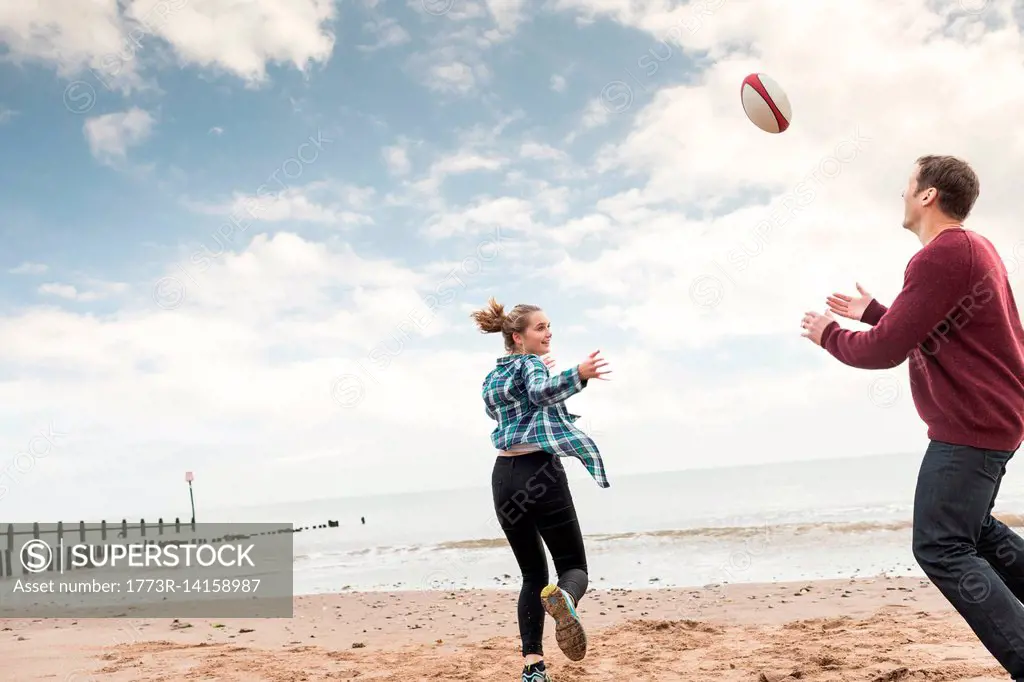 Father and daughter playing rugby on beach