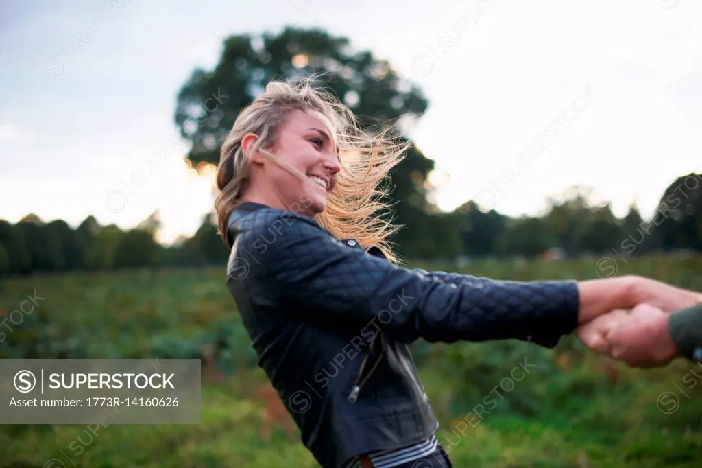 Young woman holding boyfriend's hands and spinning around in field