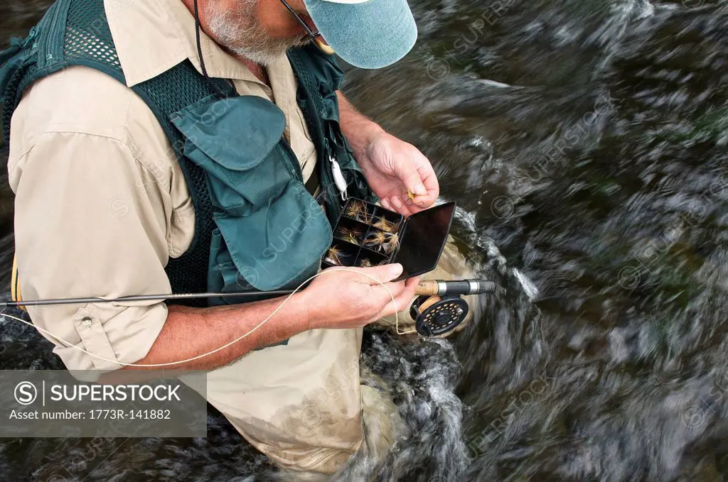 Fly fisherman holding fly box in river