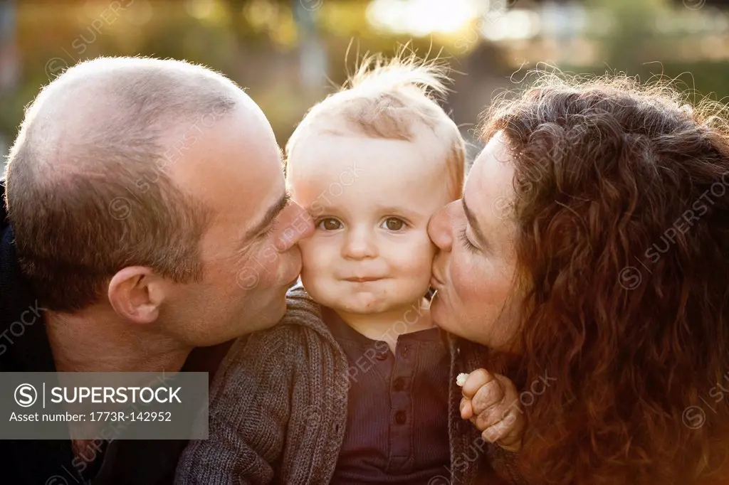 Parents kissing babys cheeks outdoors