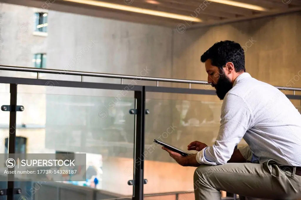 Man on mezzanine in office building using digital tablet