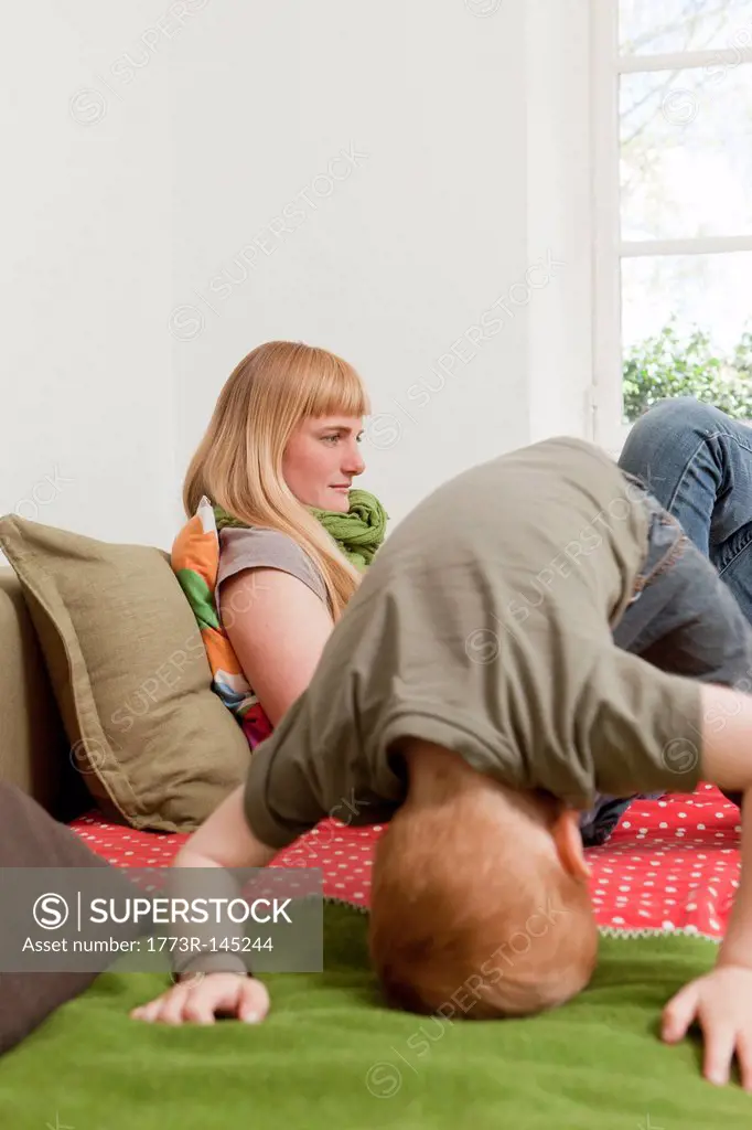 Mother relaxing as son jumps on sofa