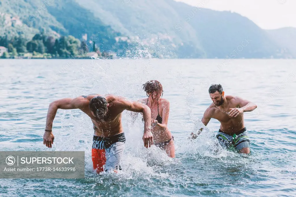 Three young adult friends play fighting in lake Como, Como, Lombardy, Italy