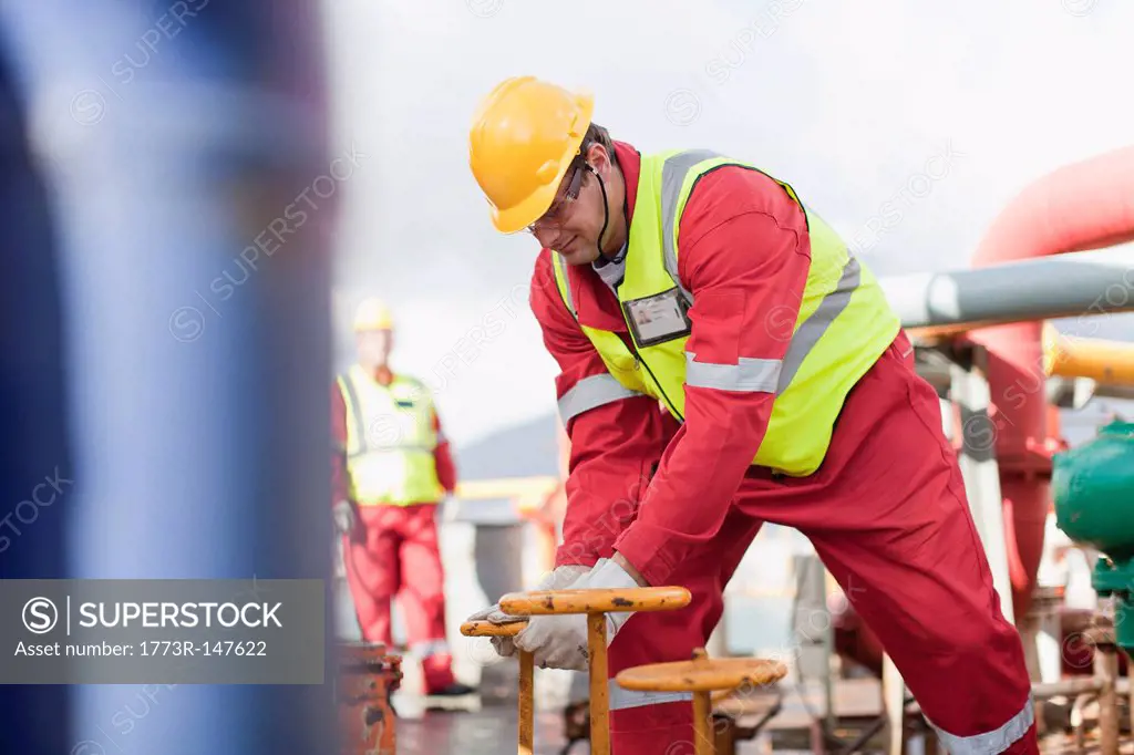 Worker turning wheel on oil rig