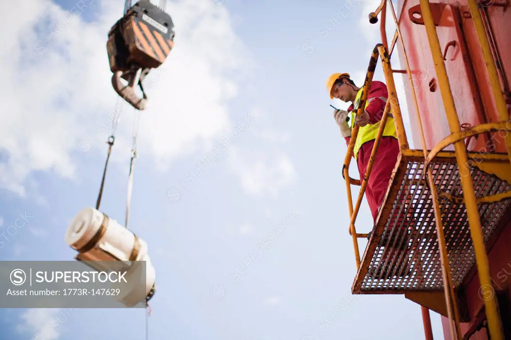 Worker directing crane on oil rig