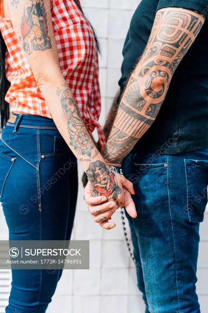 Mature tattooed hipster couple holding hands, mid section