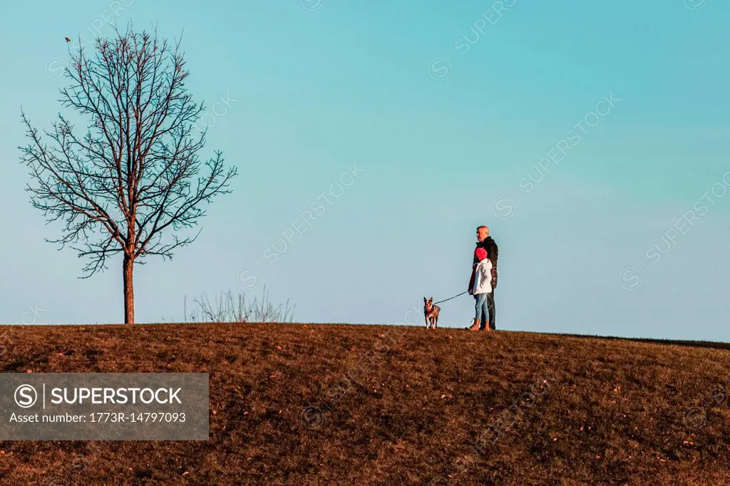 Father and daughter walking dog on hillside