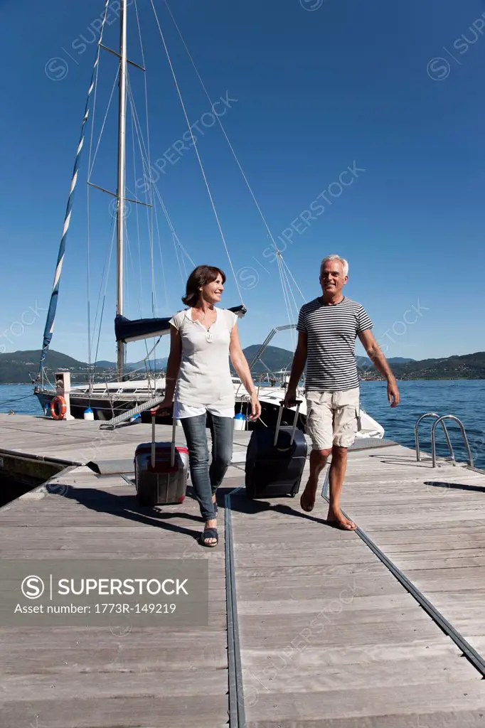 Older couple rolling luggage on pier