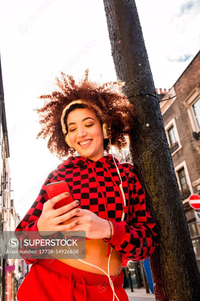Portrait of young woman outdoors, wearing headphones, holding smartphone
