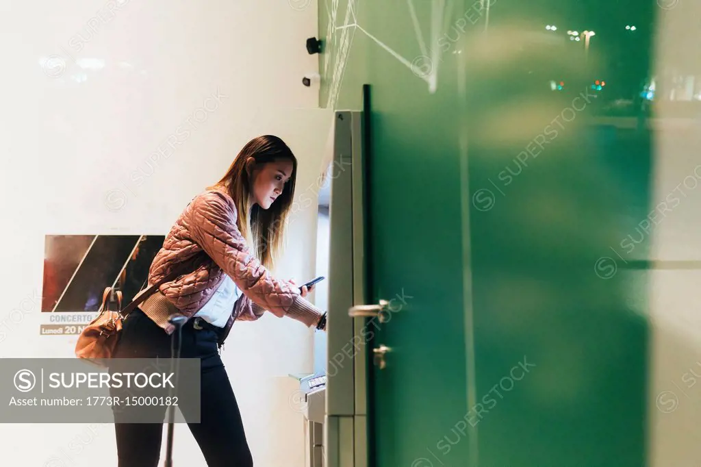 Young woman using machine to buy train ticket