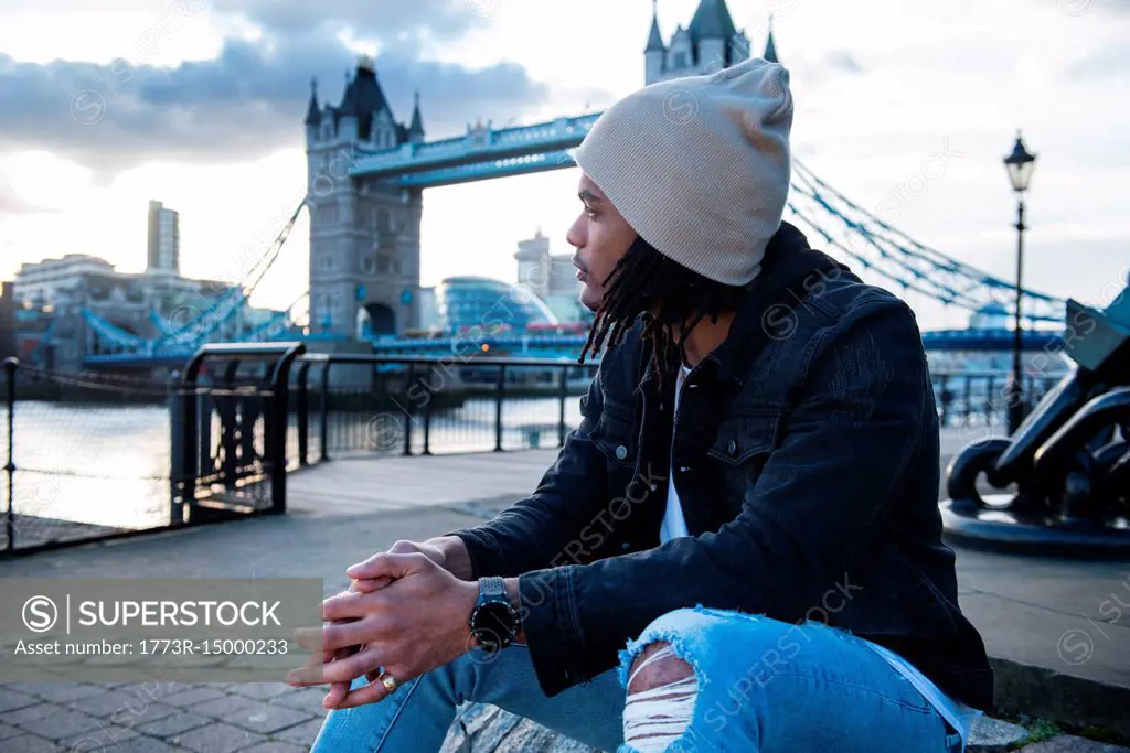 Young man sitting outdoors, pensive expressions, Tower Bridge in background, London, England, UK