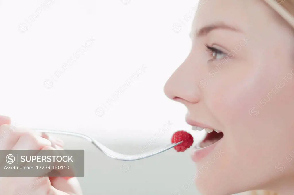 Smiling woman eating raspberry
