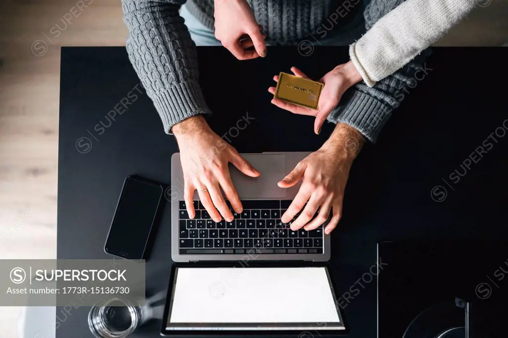Couple with credit card using laptop, overhead view, cropped
