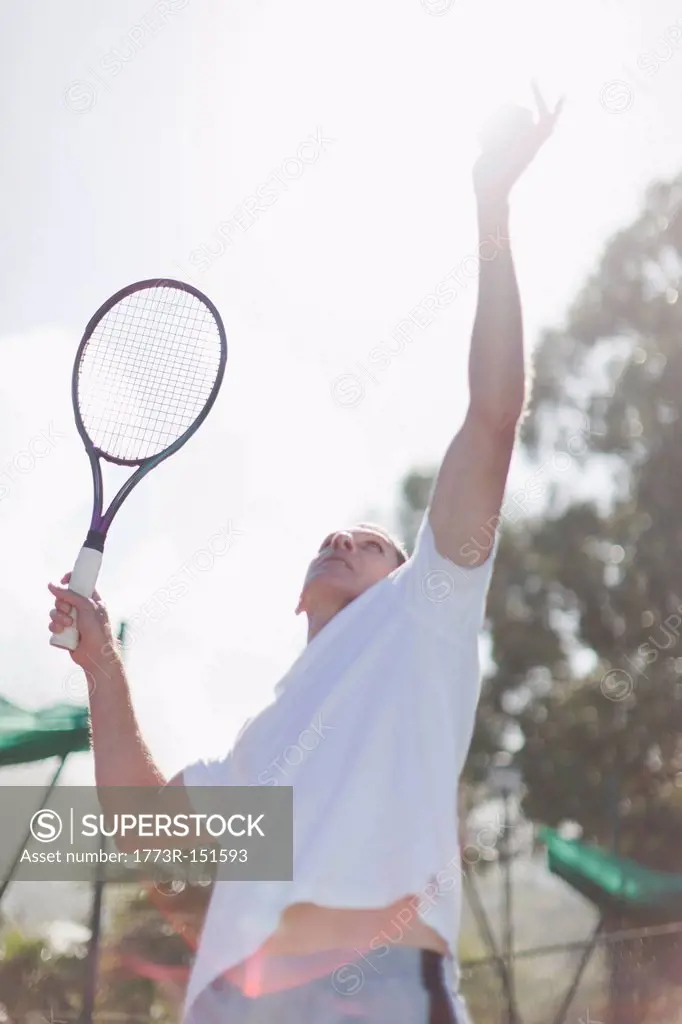 Older man serving tennis ball