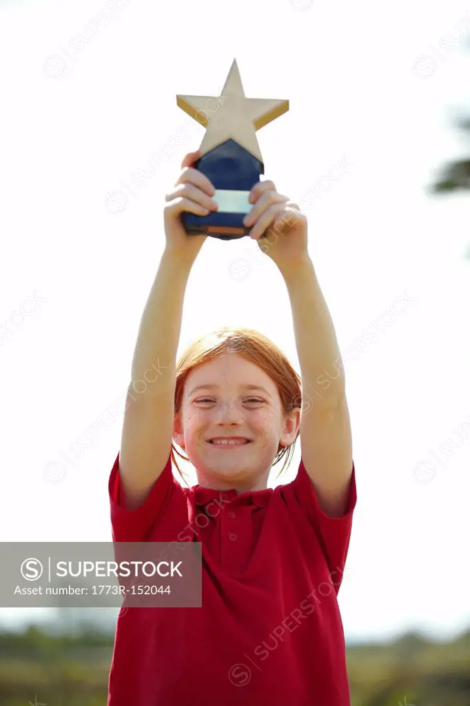 Girl cheering with trophy outdoors