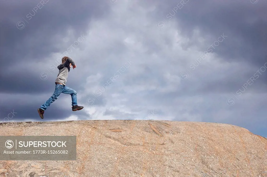 Boy running on top of rock against stormy cloud sky