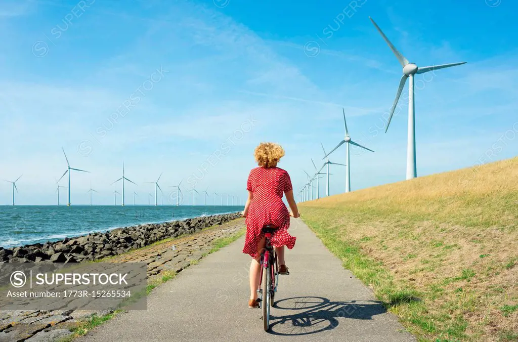 Girl cycling between onshore and offshore wind farm, Urk, Flevoland, Netherlands