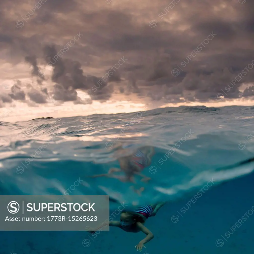 Young boy swimming underwater, split view, Tonga