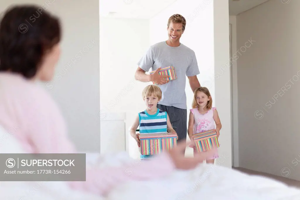 Family bringing mother presents in bed