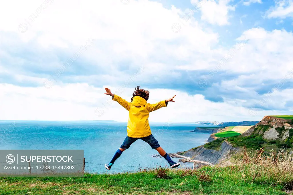 Boy jumping on clifftop by sea, Bournemouth, UK