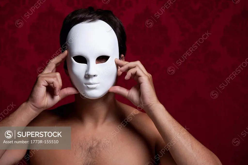 Nude man holding mask over his face