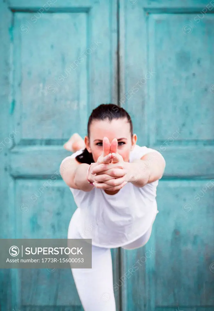 Woman practicing yoga, on one leg in front of door, portrait