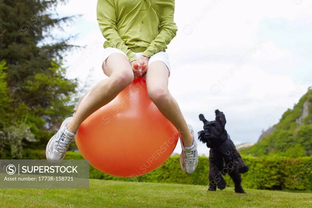 Woman on bouncy ball playing with dog