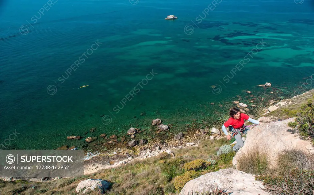 Woman climbing rocky coastal cliff