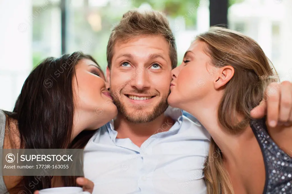 Women kissing smiling mans cheeks