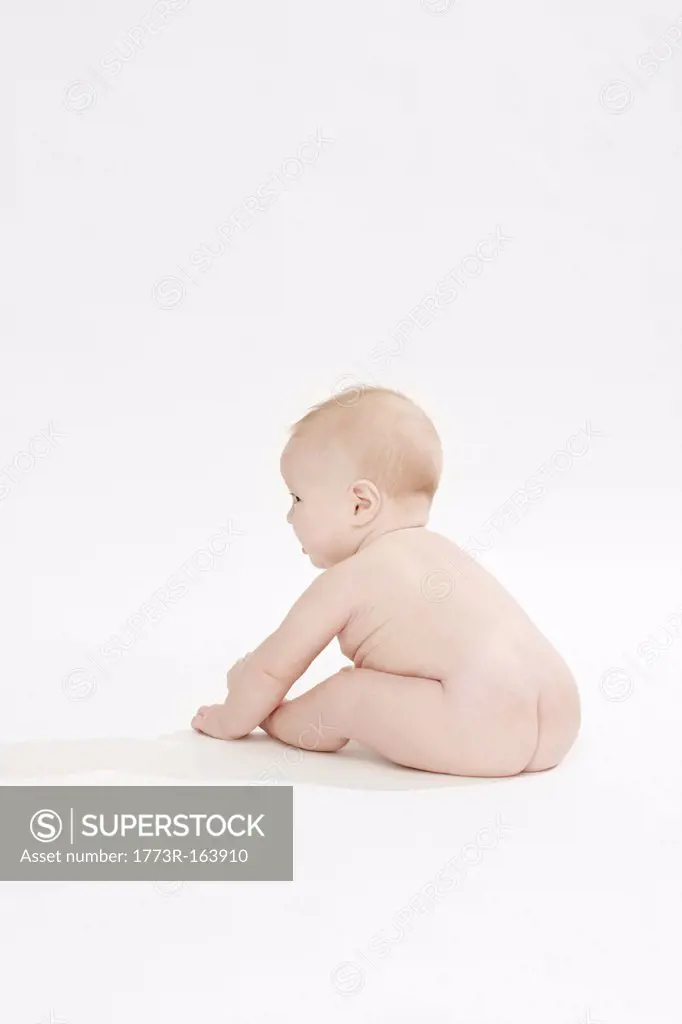 Nude baby boy sitting on floor