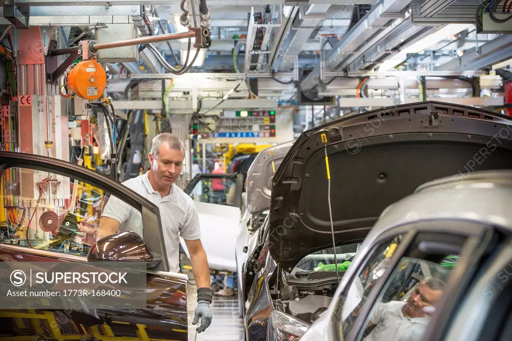 Worker fitting doors in car in car factory